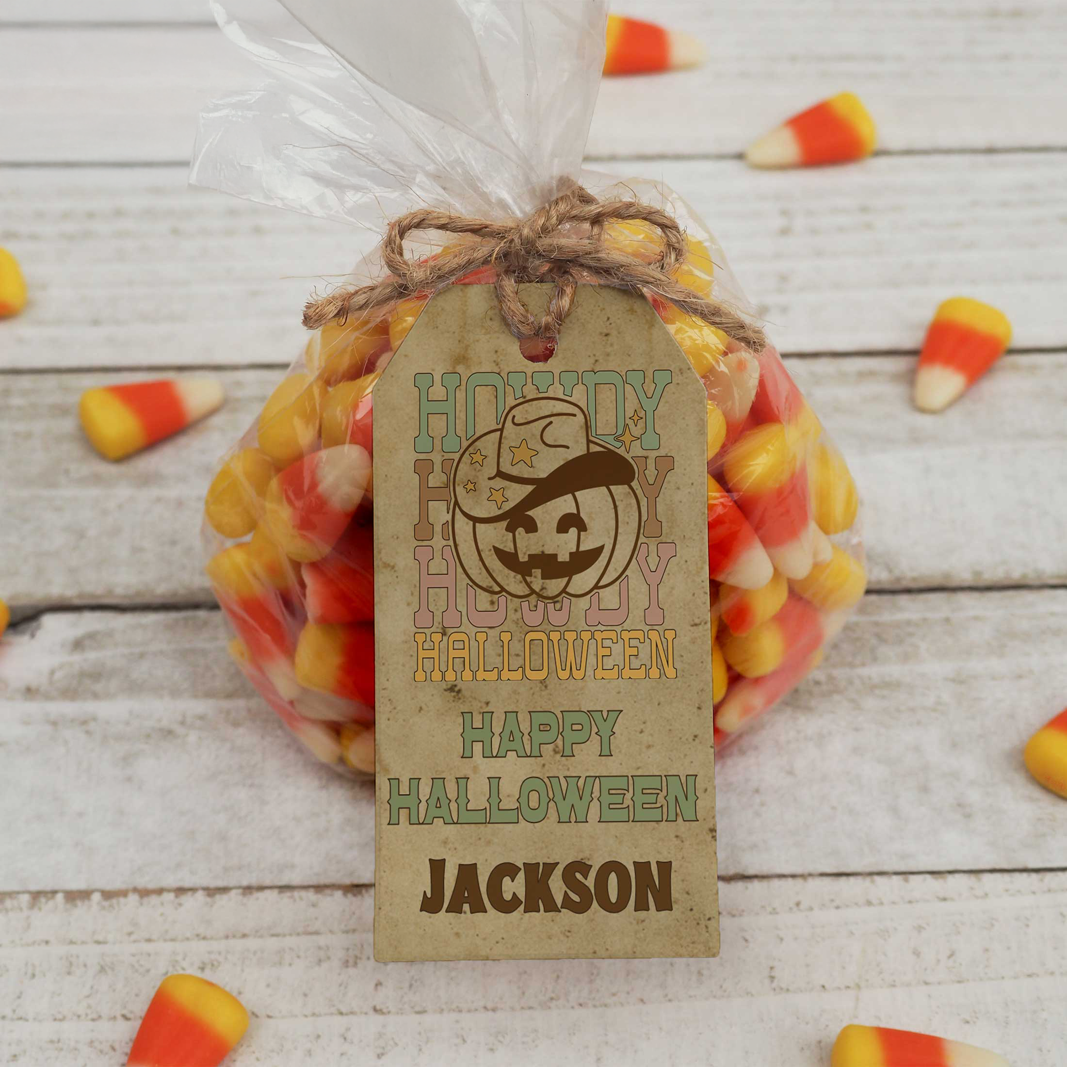 Bag of candy corn with a personalized Halloween tag on a wooden surface.